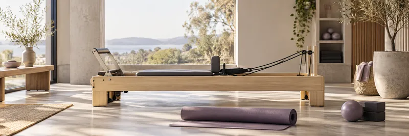 A Pilates reformer and rolled mat in a sunlit studio